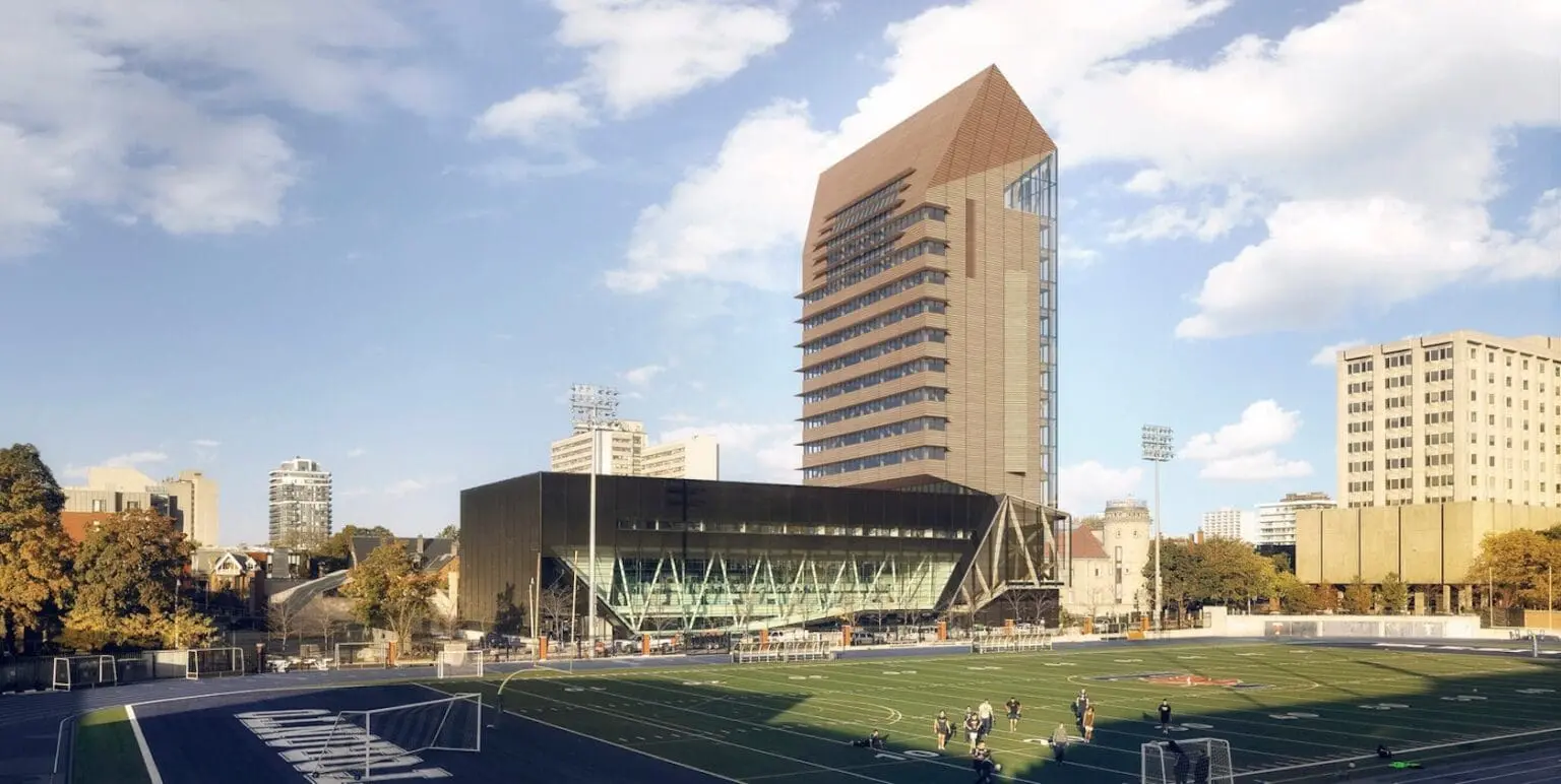 The University of Toronto Academic Tower at the Goldring Centre, featuring a modern architectural design with a glass facade and a brown sloped roof, overlooking a sports field.